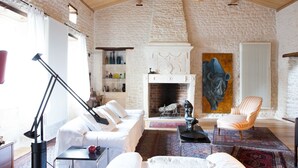 A cozy living room with a fireplace, white furniture, and a stone wall. - La Bribaudonnière (Saint-Palais-de-Phiolin)