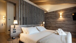 A modern hotel room with a wooden headboard, two bedside lamps, a flat-screen TV, and a neatly made bed. - Hotel delle Alpi (Vermiglio)