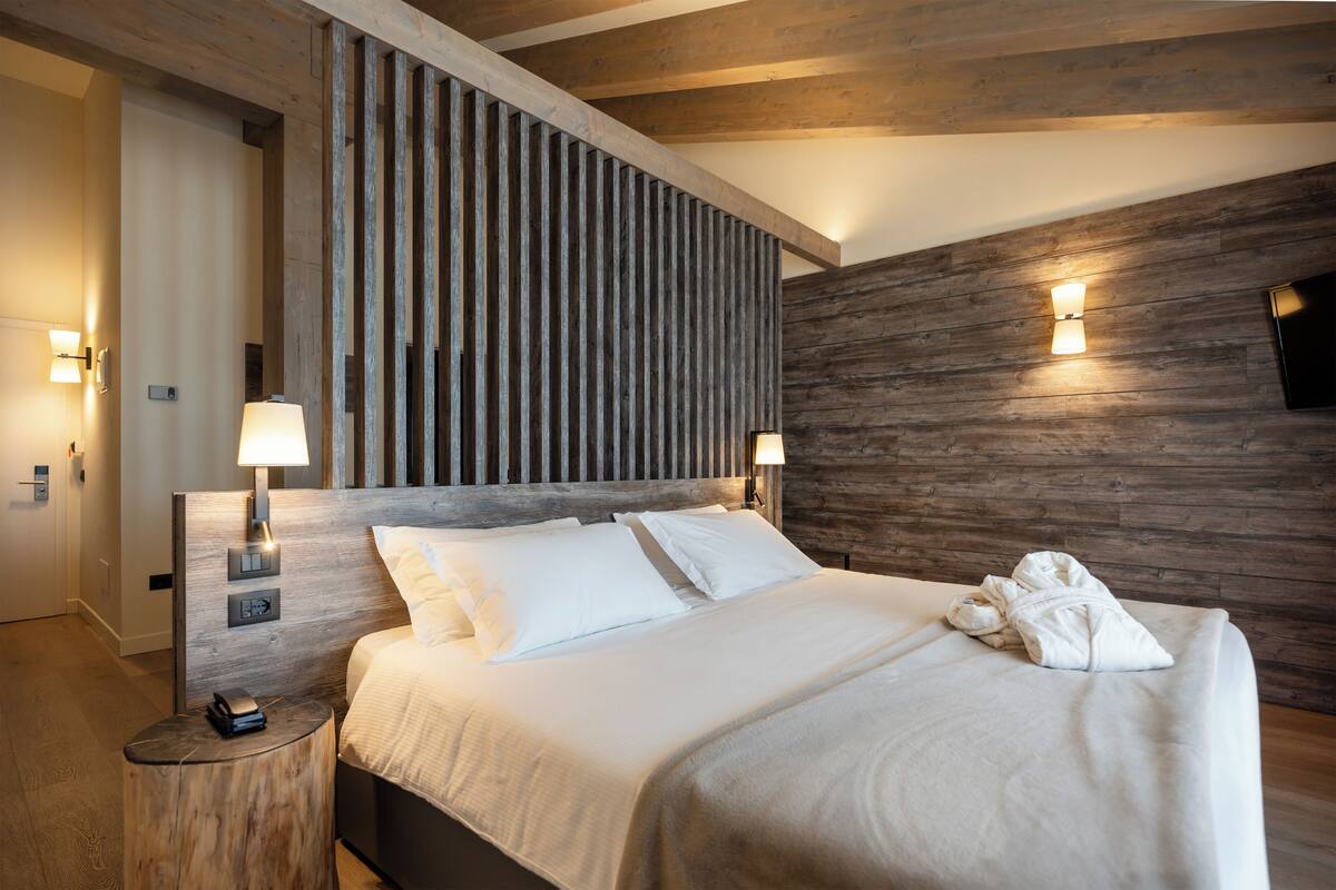 A modern hotel room with a wooden headboard, two bedside lamps, a flat-screen TV, and a neatly made bed.