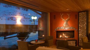 Un interior acogedor con chimenea, asientos cómodos y un amplio ventanal con vistas a un paisaje nevado.