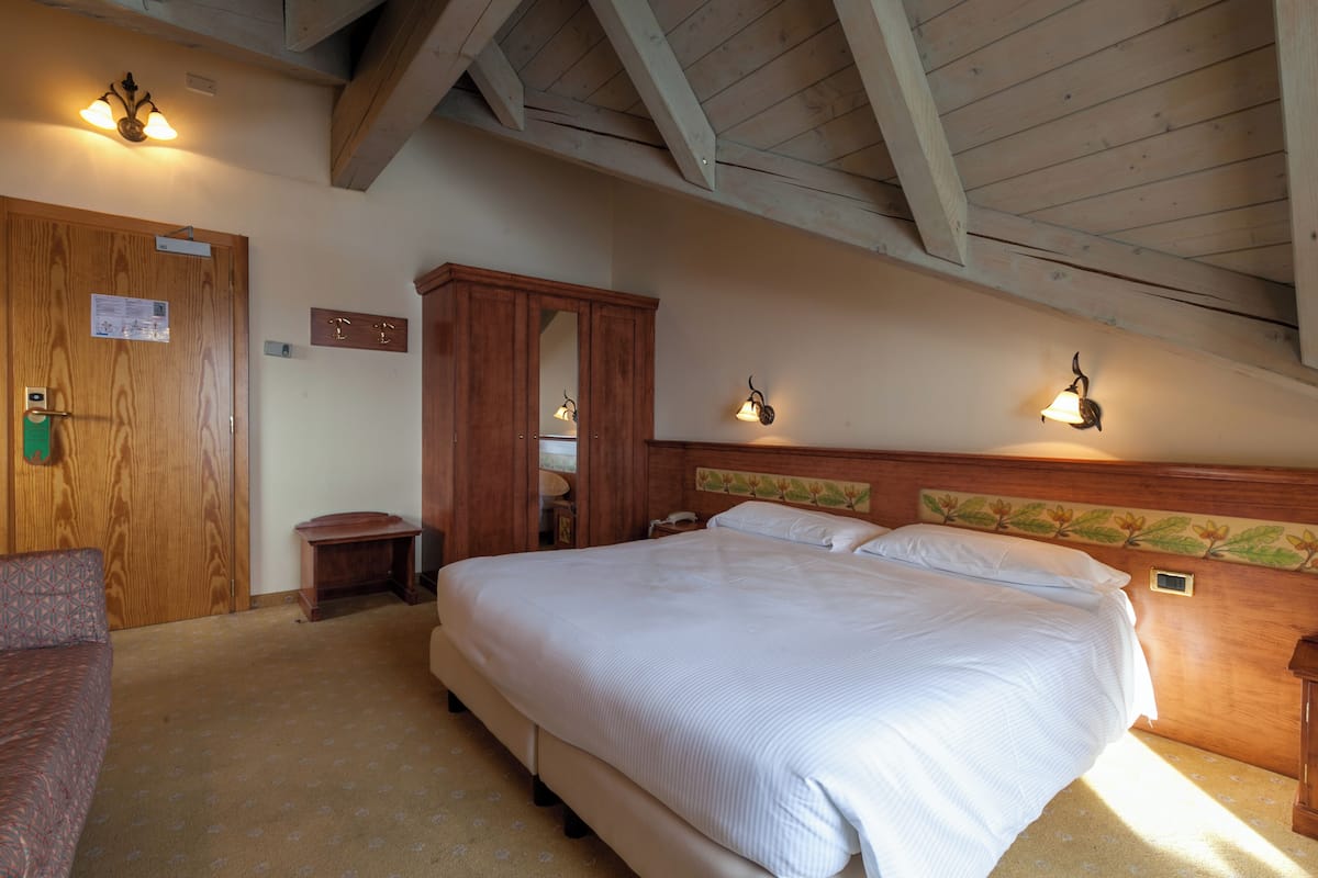 A bedroom with a large bed, wooden headboard, two bedside lamps, a wooden wardrobe, and a small bedside table.
