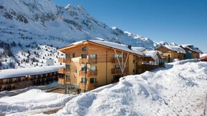 Un complejo turístico en la montaña cubierto de nieve, con edificios de madera, balcones y una vista despejada de las montañas.
