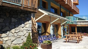 Un hotel con fachada de piedra, balcones de madera y mesas al aire libre.