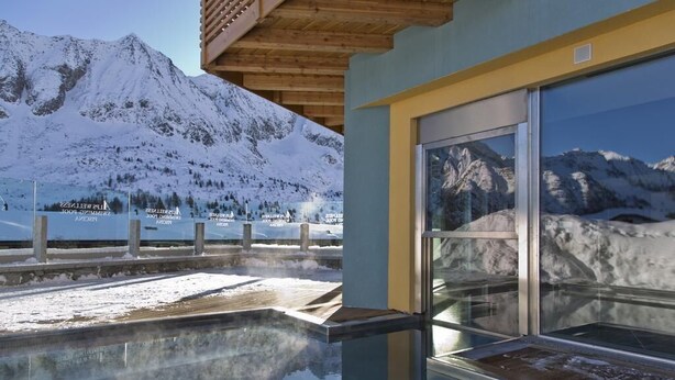 Un edificio moderno con piscina de cristal que refleja montañas nevadas.