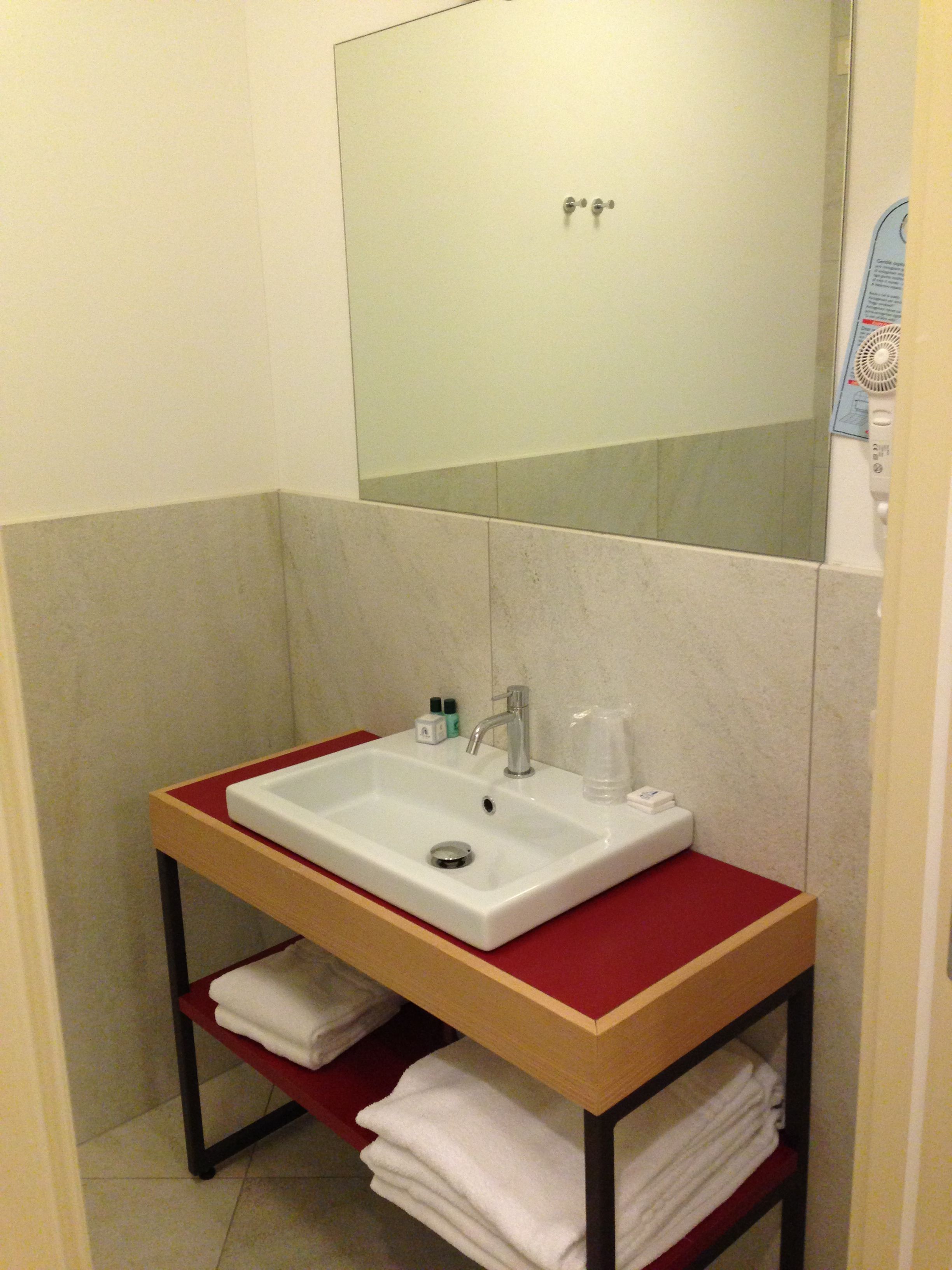 A bathroom with a white sink, a mirror, and a red shelf with towels.