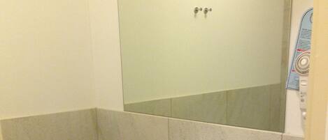 A bathroom with a white sink, a mirror, and a red shelf with towels.