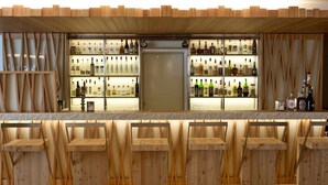 Zona de bar con taburetes de madera y estantes llenos de botellas de licor.