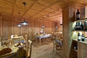 A wooden dining area with tables set for a meal, wooden walls, and hanging pendant lights. - Hotel delle Alpi (Vermiglio)