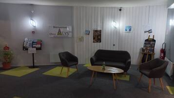 A reception area with a black sofa, two chairs, a small round table, and a sign reading "Bienvenue Chez Alys Bourg en Bresse Sud".