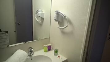 A bathroom with a white sink, a mirror, and a hairdryer mounted on the wall. There are toiletries on the sink counter.