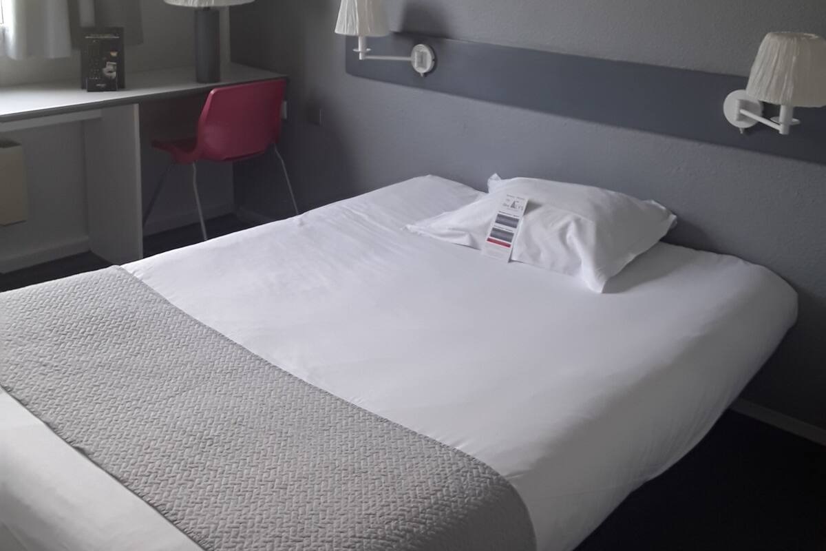 Ein Hotelzimmer mit Bett, Schreibtisch, Stuhl und einer wandmontierten Klimaanlage.