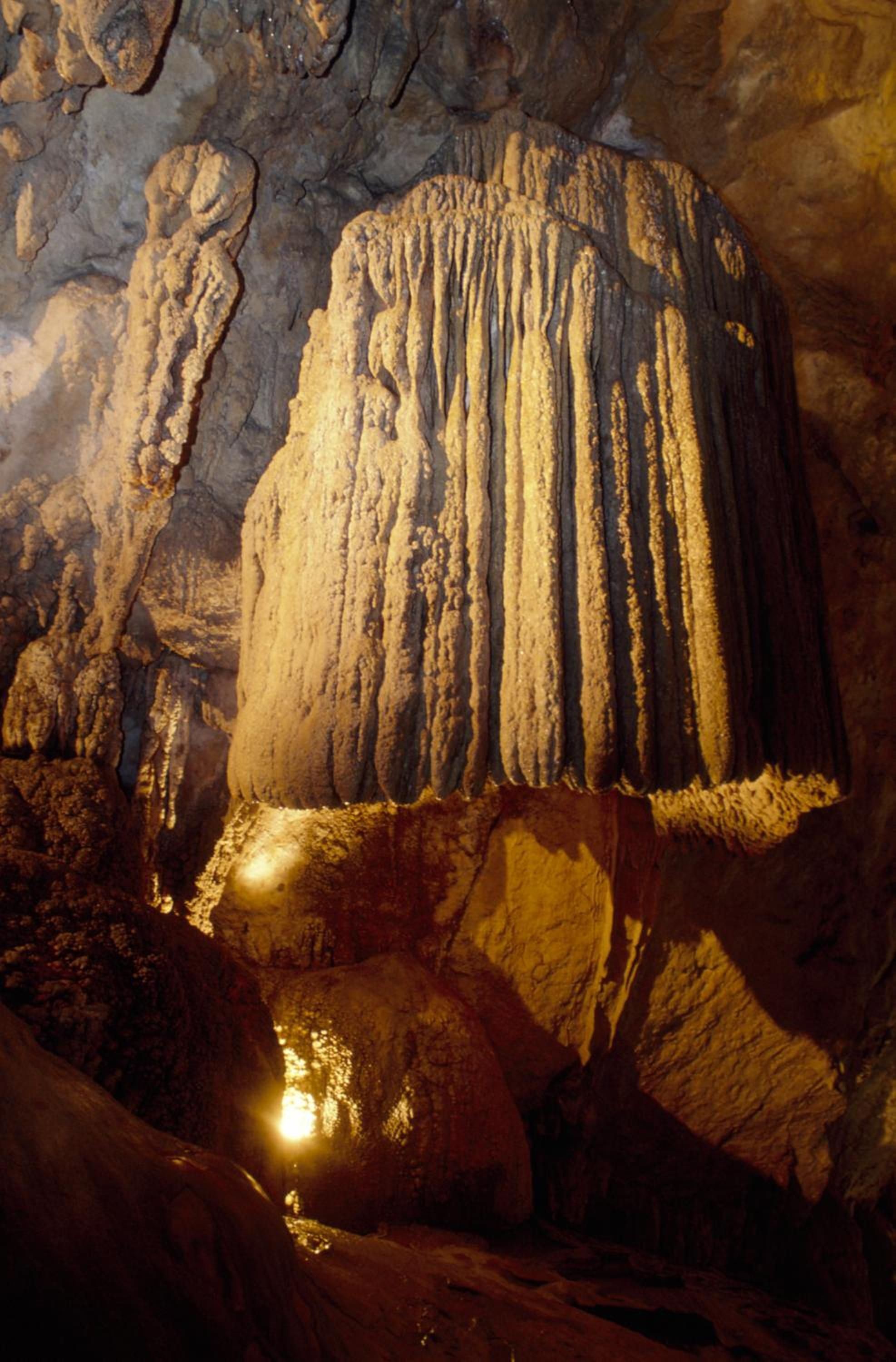 A cave with stalactites and stalagmites, illuminated by artificial lighting.