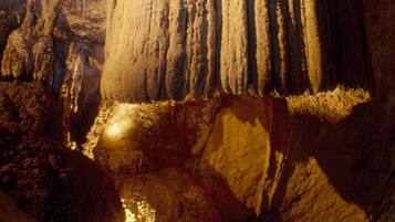 A cave with stalactites and stalagmites, illuminated by artificial lighting.