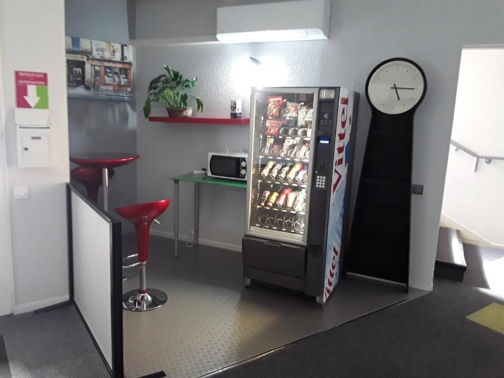 A kitchenette with a microwave, a vending machine, a clock, and a red bar stool.