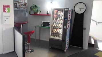 A kitchenette with a microwave, a vending machine, a clock, and a red bar stool.