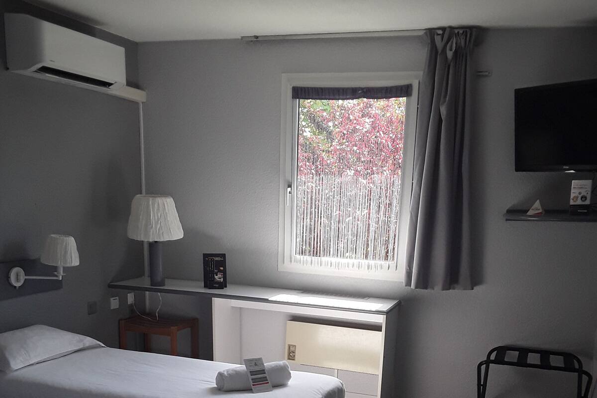 Ein Hotelzimmer mit zwei Betten, einem Schreibtisch, einem Stuhl, einem Fernseher und einem Fenster mit Vorhängen.