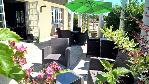 An outdoor patio with wicker furniture, a green umbrella, and potted plants.
