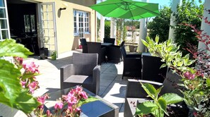 Un patio al aire libre con mobiliario de mimbre, una sombrilla verde y plantas en macetas.