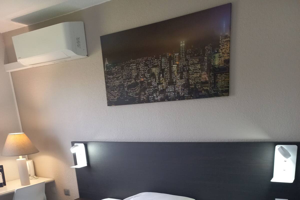 Ein Hotelzimmer mit einem großen Bett, einem Schreibtisch mit Lampe und einem Stadtbild an der Wand.