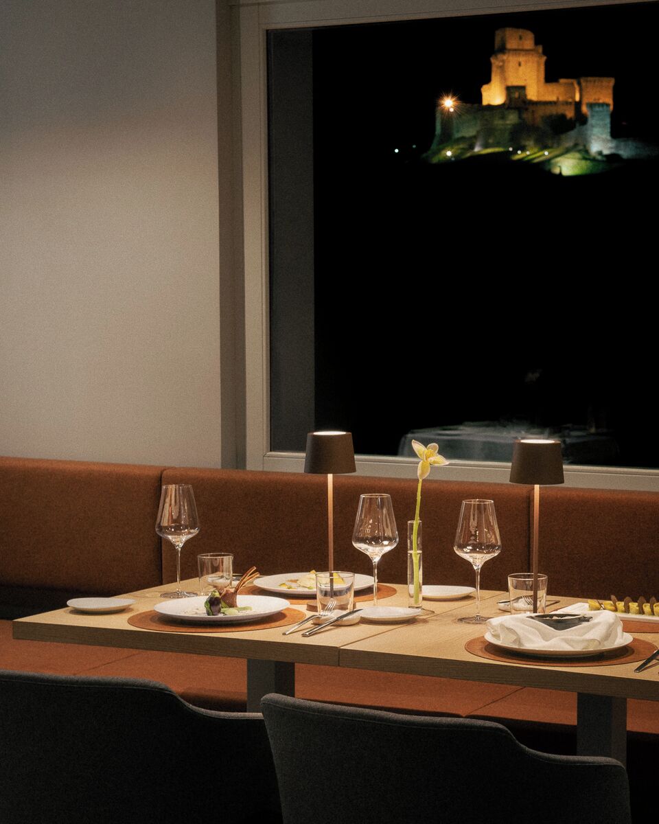 A dining table set with plates, glasses, and cutlery, with a window view of a castle at night.