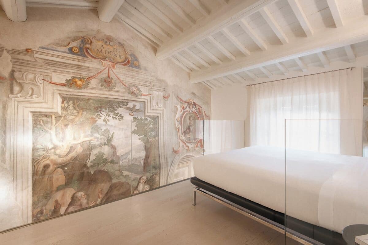 A bedroom with a large mural, a bed, and a ceiling with exposed beams.