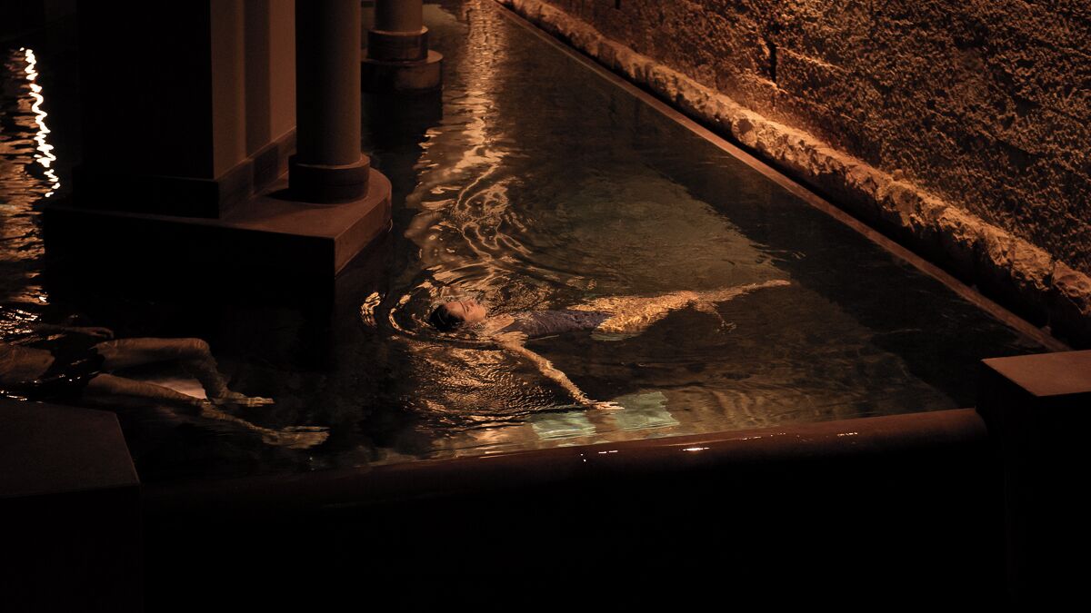 Vista nocturna de una piscina con fuentes y arquitectura de piedra.