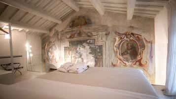 Ein Schlafzimmer mit einem großen Bett, Deckenbalken, einem Wandgemälde und einem gerahmten Porträt an der Wand.