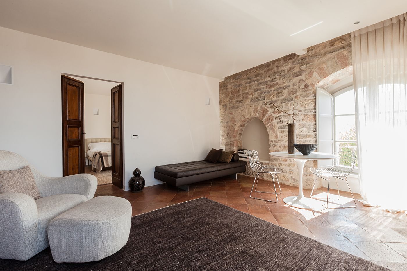 Una sala de estar moderna con una pared de piedra, un sofá, una mesa de comedor con sillas y un ventanal grande.