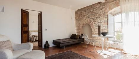 A modern living room with a stone wall, a sofa, a dining table with chairs, and a large window.