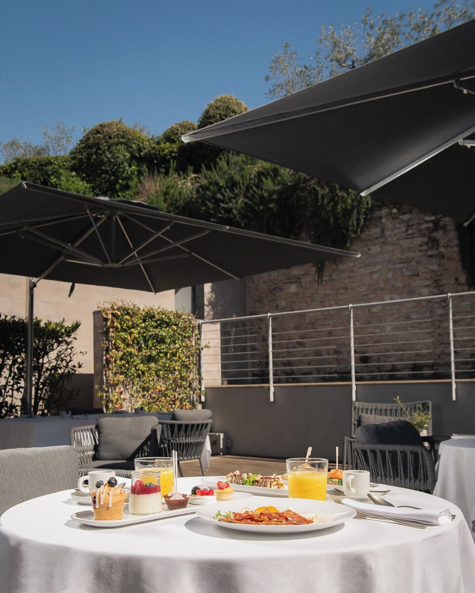 An outdoor dining area with tables, umbrellas, and a stone wall in the background.