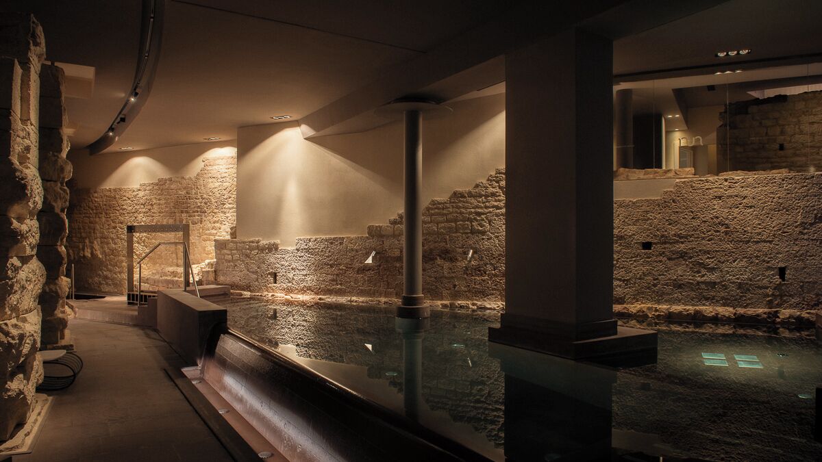 A historical site with stone walls, a central water feature, and a modern glass barrier.