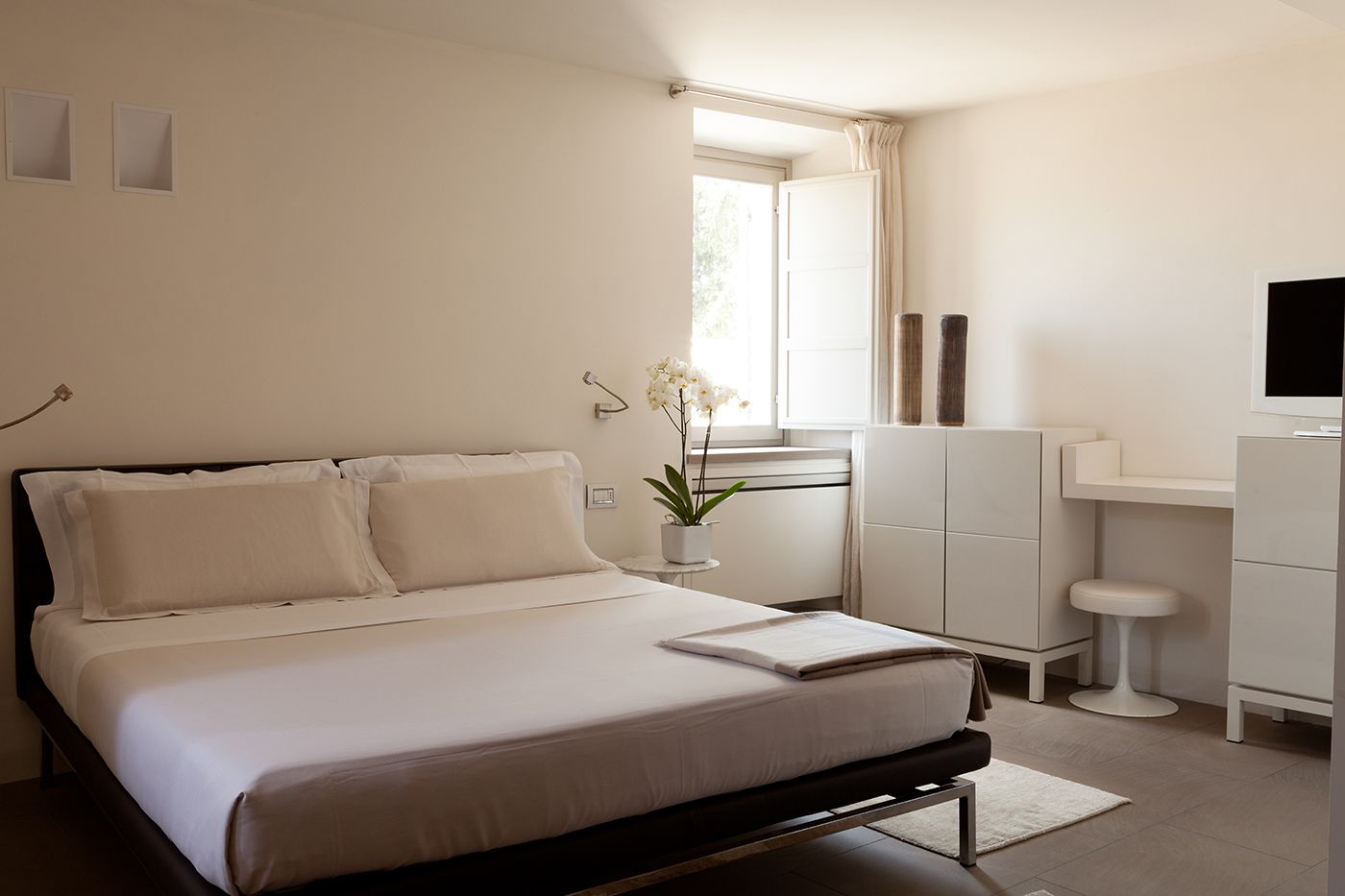A modern bedroom with a bed, bedside table, potted plant, and a TV on a stand.