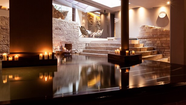 Un espace spa moderne doté d’un bassin aux reflets changeants, d’escaliers en pierre et de bougies.