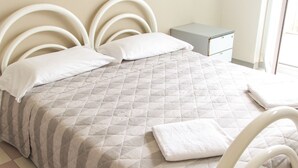 A neatly made bed with a quilted bedspread and pillows, a bedside table, and a nightstand. - Ostello di Bergamo (Bergamo)