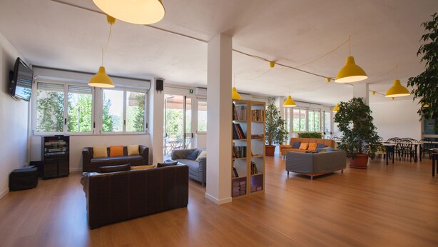 A spacious living area with wooden flooring, a sofa, a coffee table, and a bookshelf. - Ostello di Bergamo (Bergamo)