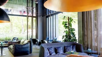 Un espacio lounge moderno con un sofá grande, sillones y una mesa de centro. Amplias ventanas ofrecen luz natural y vistas a zonas verdes.