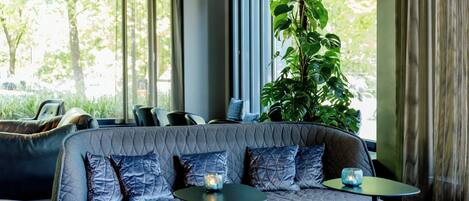 Um interior moderno com uma ampla área de assentos acolchoados, uma planta em vaso e vista para o verde lá fora.