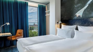 Ein Hotelzimmer mit einem großen Bett, einem Schreibtisch mit Stuhl, einem Fenster mit Vorhängen und einem Wandbild einer Rakete.