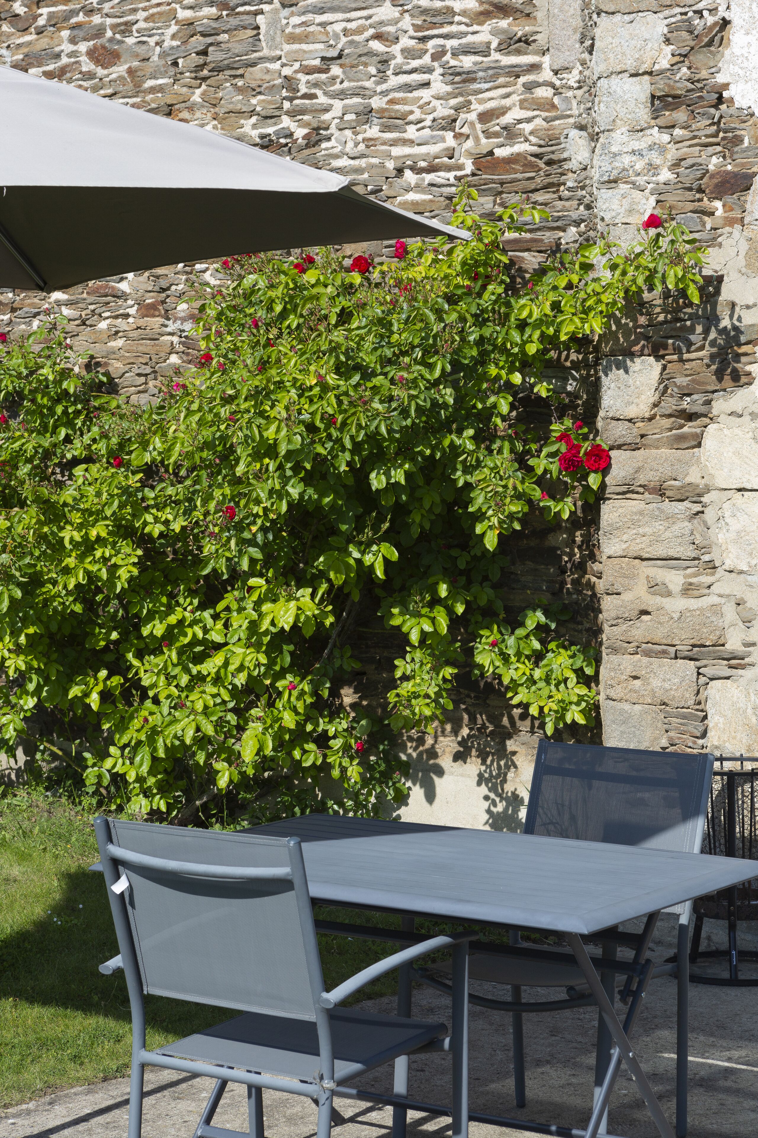 A patio with a table and chairs, a stone wall, and a bush with red flowers.