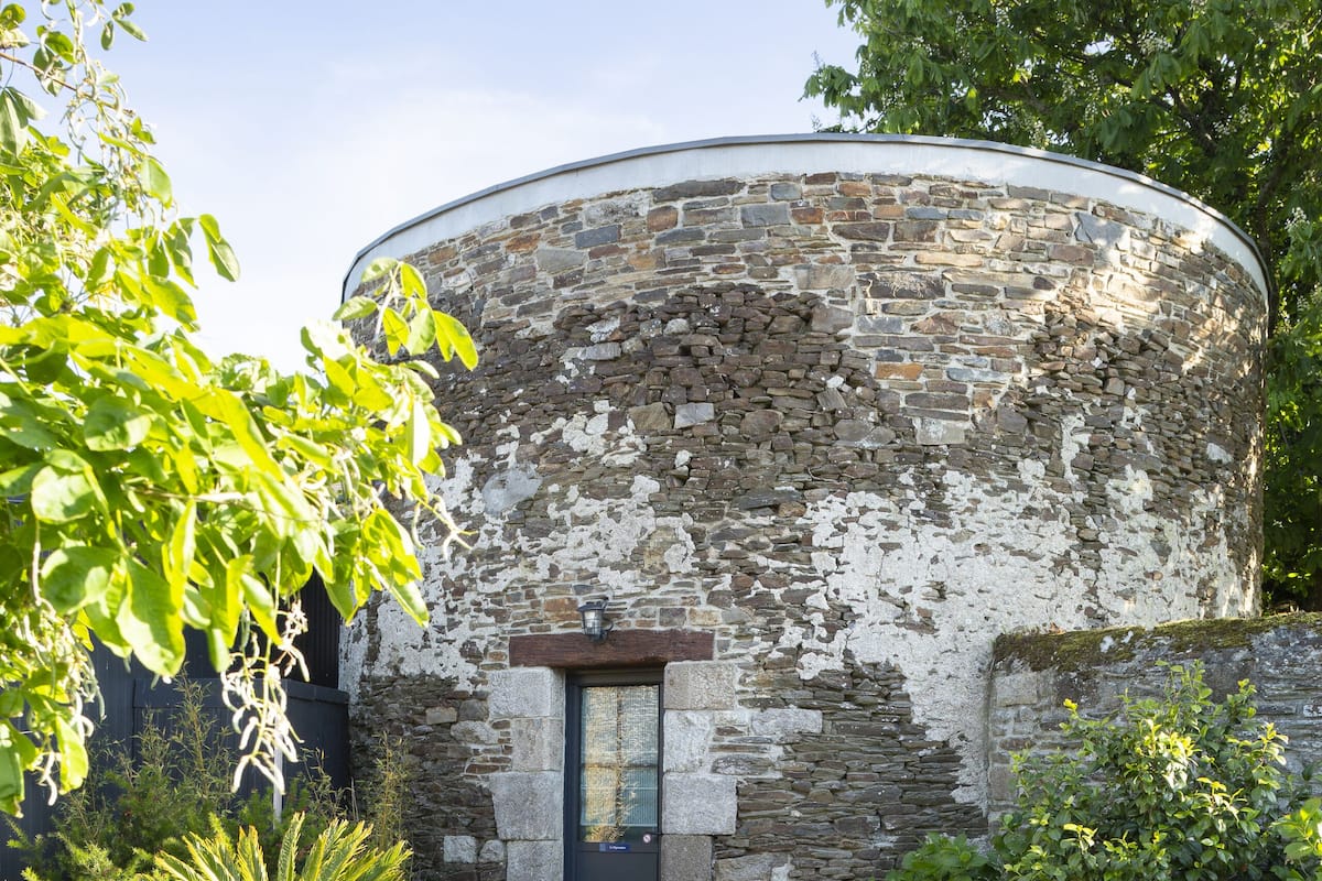Ein rundes Steinhaus mit einer Tür und zwei Liegestühlen im Vordergrund.
