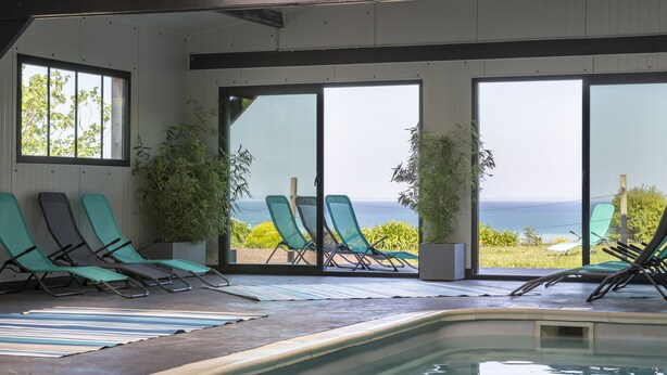 An indoor swimming pool area with lounge chairs and large windows offering a view of the ocean. - Les Chambres de la Métairie du Vauhariot (Cancale)