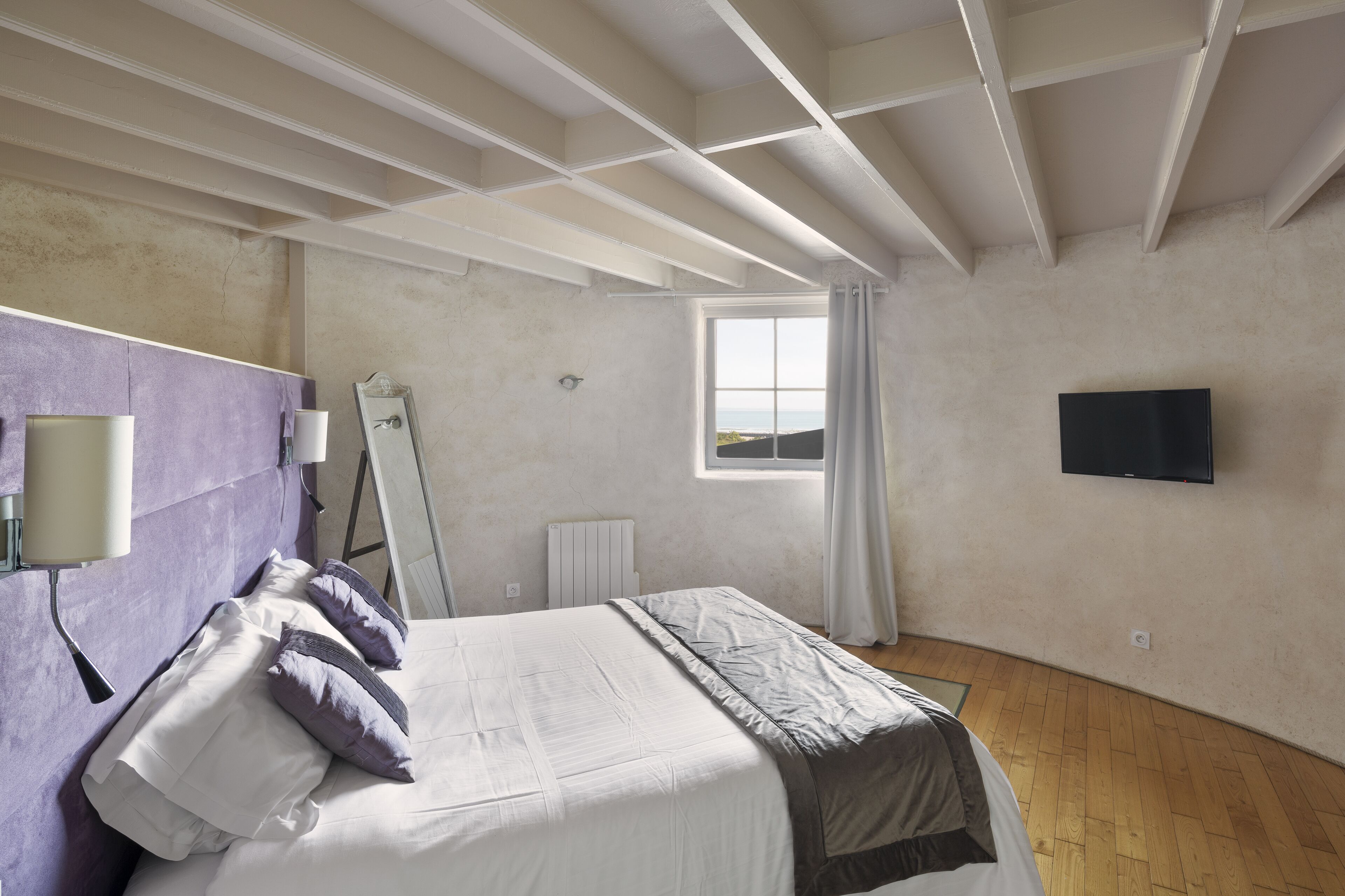 A bedroom with a bed, a window, a flat-screen TV, and a radiator.