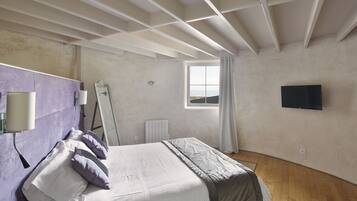 A bedroom with a bed, a window, a flat-screen TV, and a radiator.