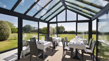 Een oranjerie met glazen wanden, tafels gedekt voor het diner en stoelen.
