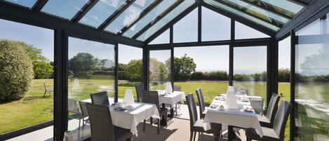 A conservatory with glass walls, tables set for dining, and chairs.