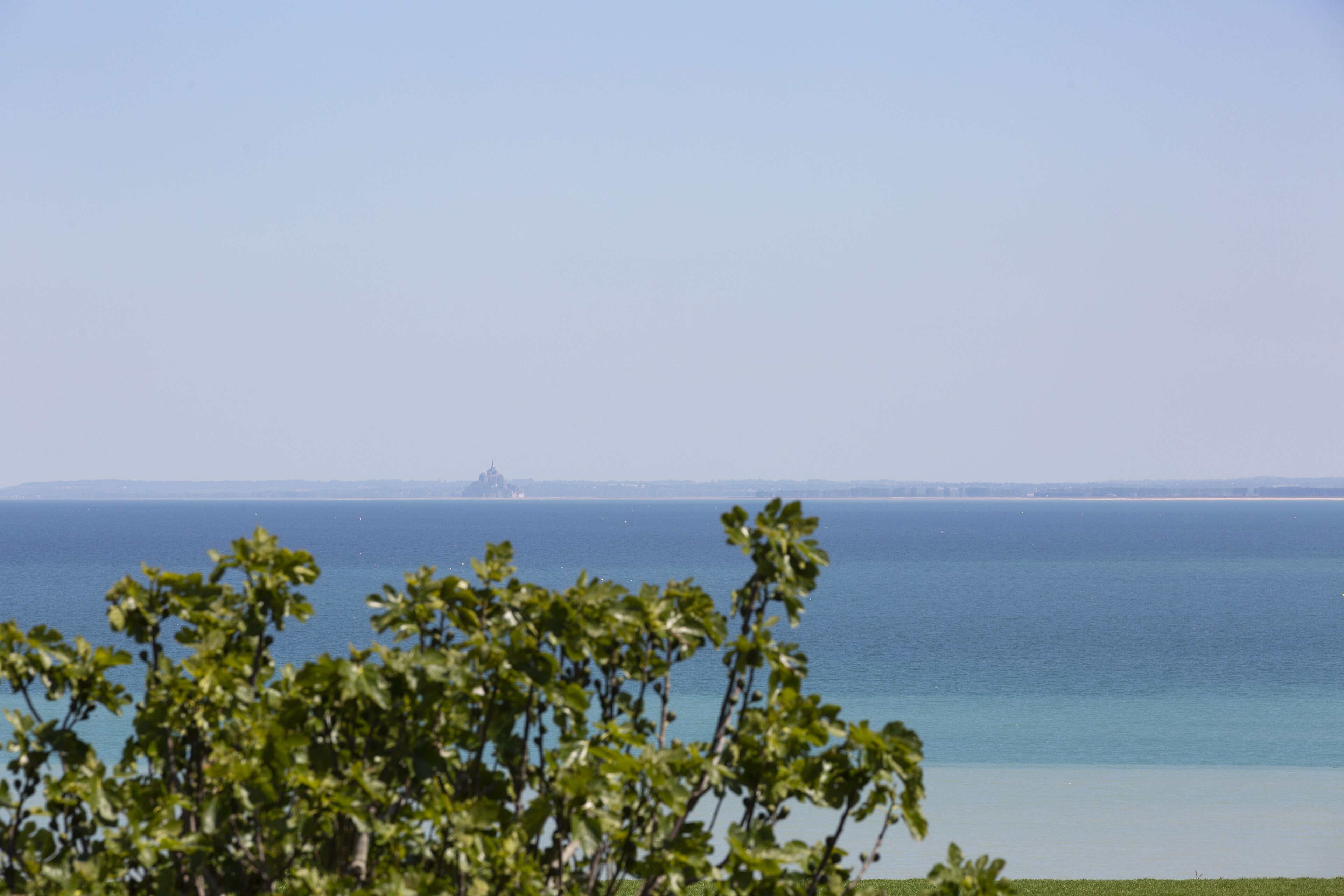 A coastal view with a clear sky, a calm sea, and distant land.