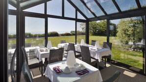 A conservatory with tables set for dining, large windows, and a view of the outdoors. - Les Chambres de la Métairie du Vauhariot (Cancale)