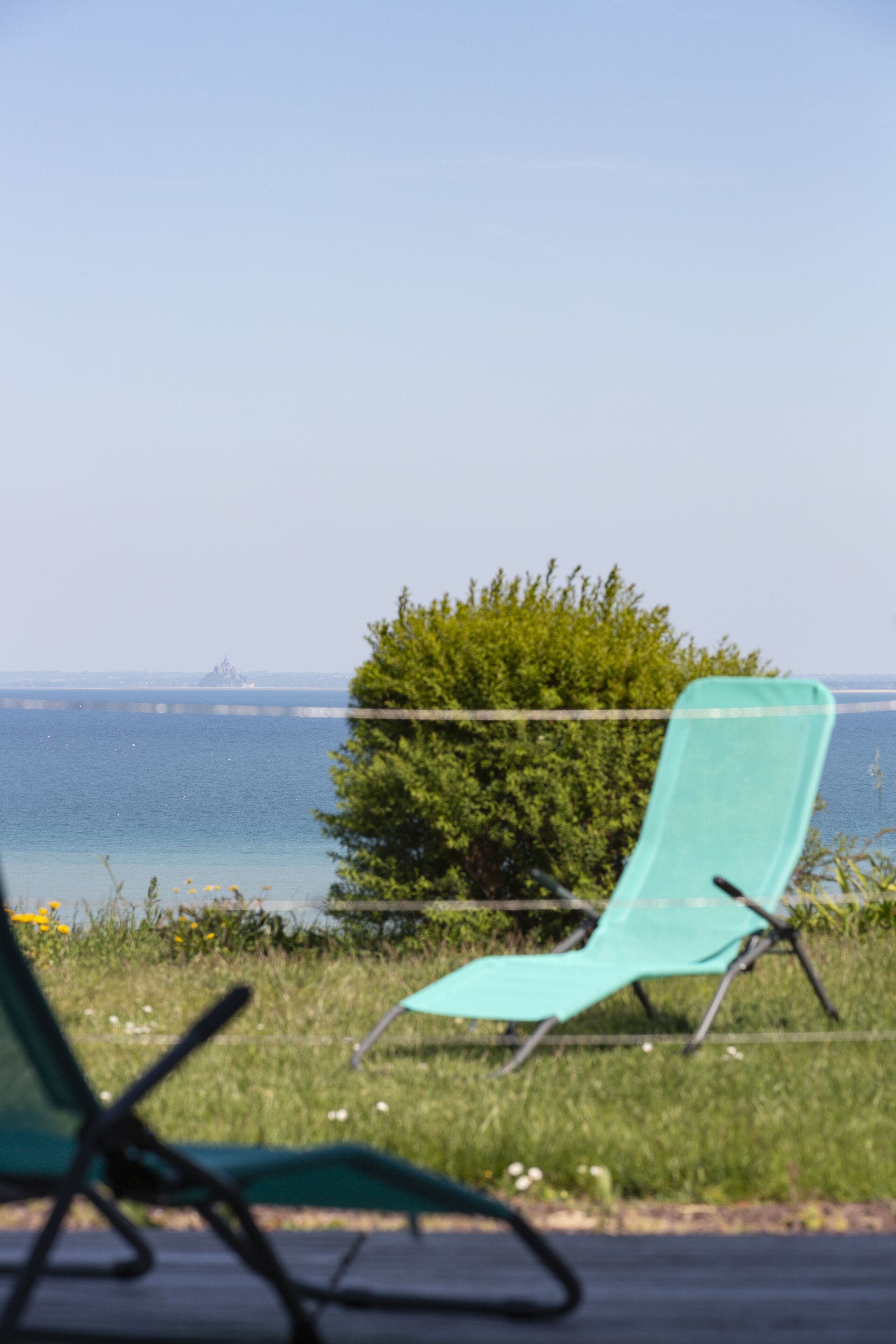 Blick auf einen Strand mit einem türkisfarbenen Liegestuhl und einem grünen Busch im Vordergrund.