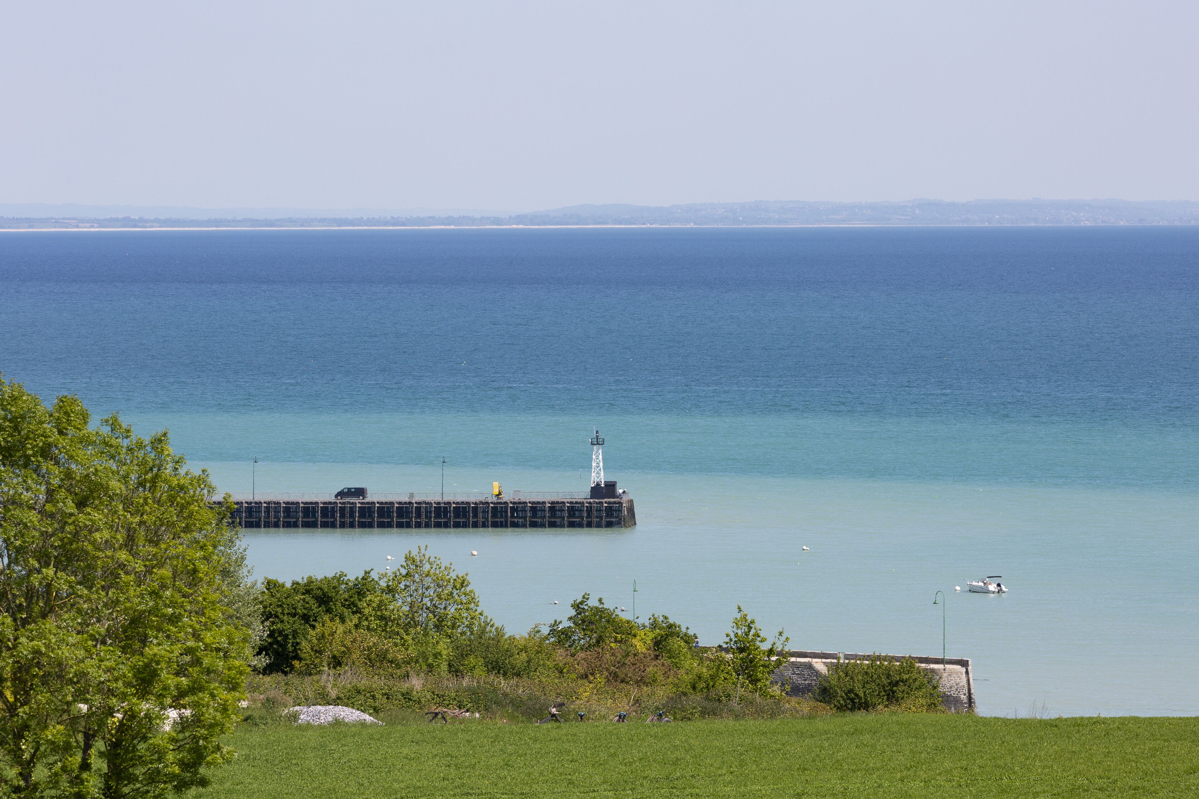 A coastal view with a lighthouse, pier, and calm sea.