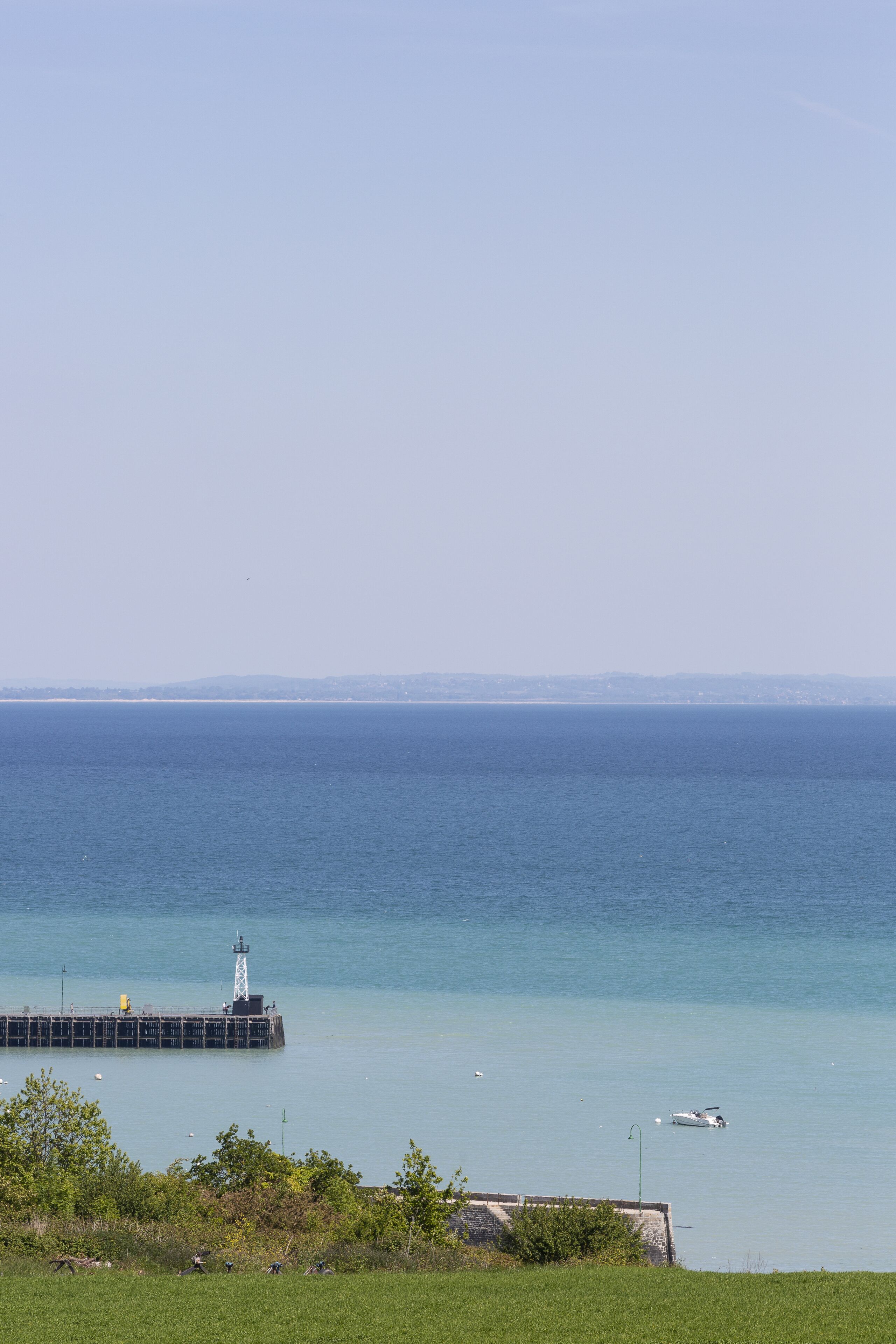 A coastal scene with a pier extending into the sea, a lighthouse, and a clear sky.